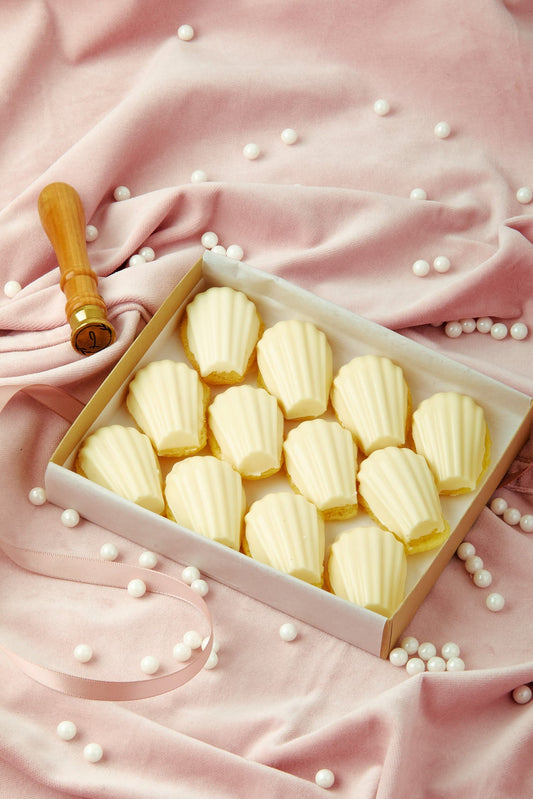 Box of madeleines on a pink fabric background with white pearls