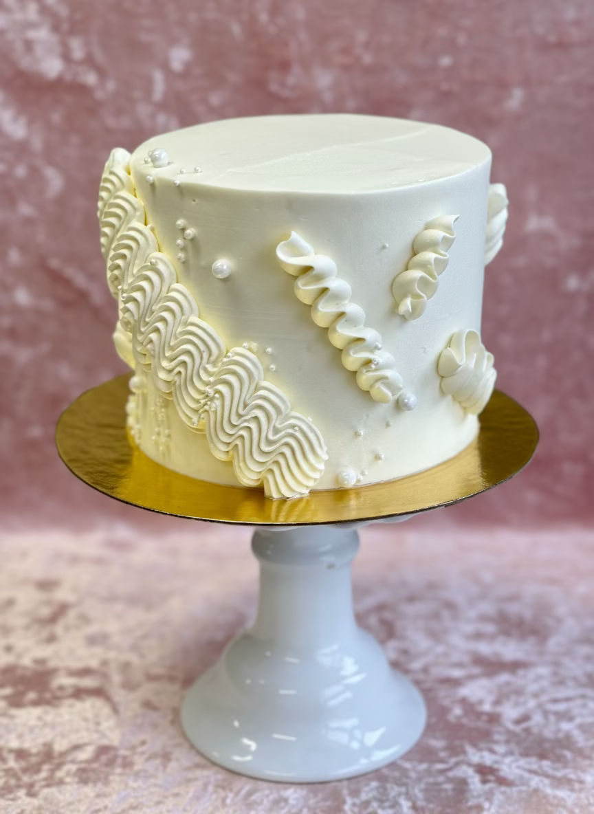 White cake with decorative patterns on a gold cake stand against a neutral background